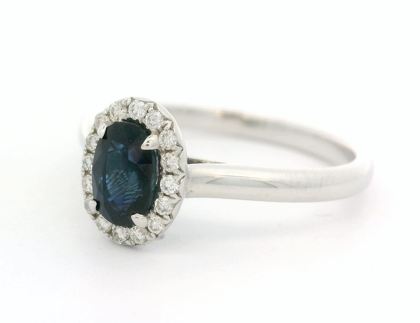 18 karaat witgouden Halo rozet ring van 2.74 gram. Bezet met 1 ovaal geslepen saffier van 0.80 crt en 16 briljant geslepen diamanten met een totaalgewicht van 0.12 crt. Kleur: G Kwaliteit: VS Zetting: 9 x 7 mm Model: R 10448