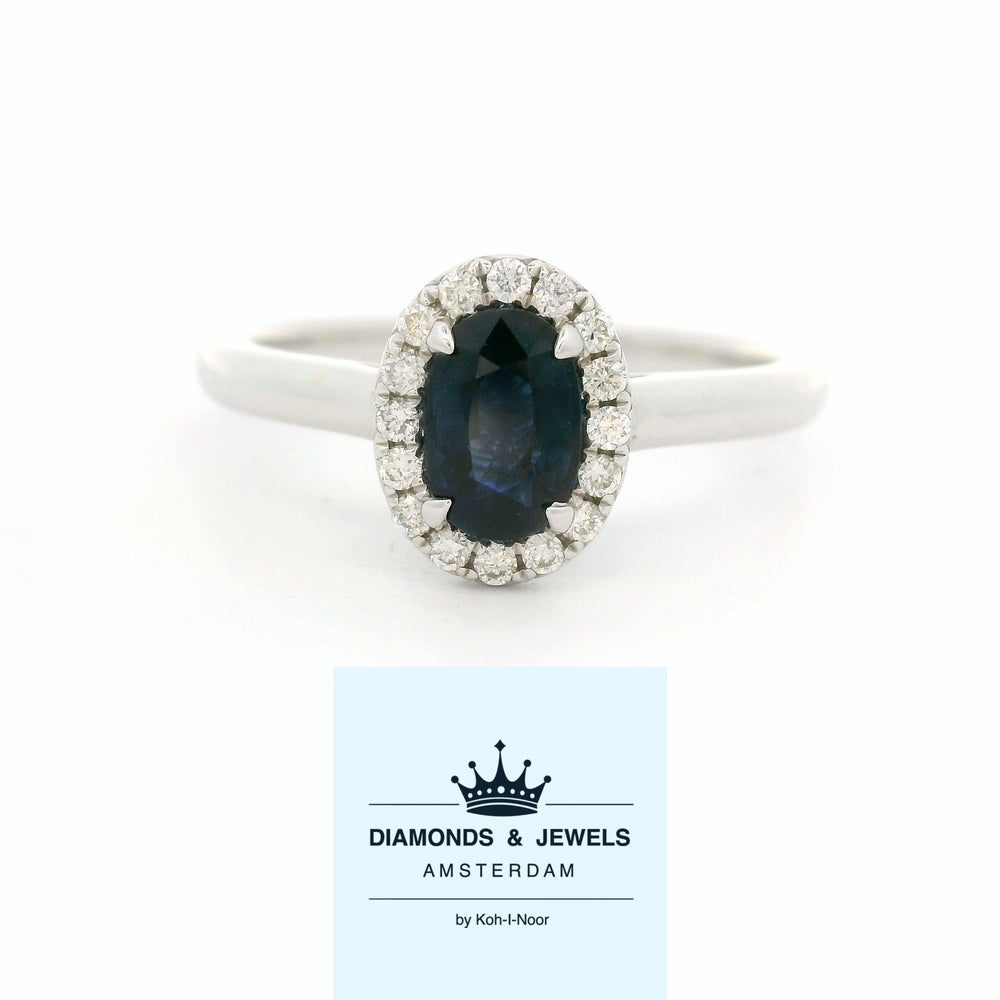 18 karaat witgouden Halo rozet ring van 2.74 gram. Bezet met 1 ovaal geslepen saffier van 0.80 crt en 16 briljant geslepen diamanten met een totaalgewicht van 0.12 crt. Kleur: G Kwaliteit: VS Zetting: 9 x 7 mm Model: R 10448