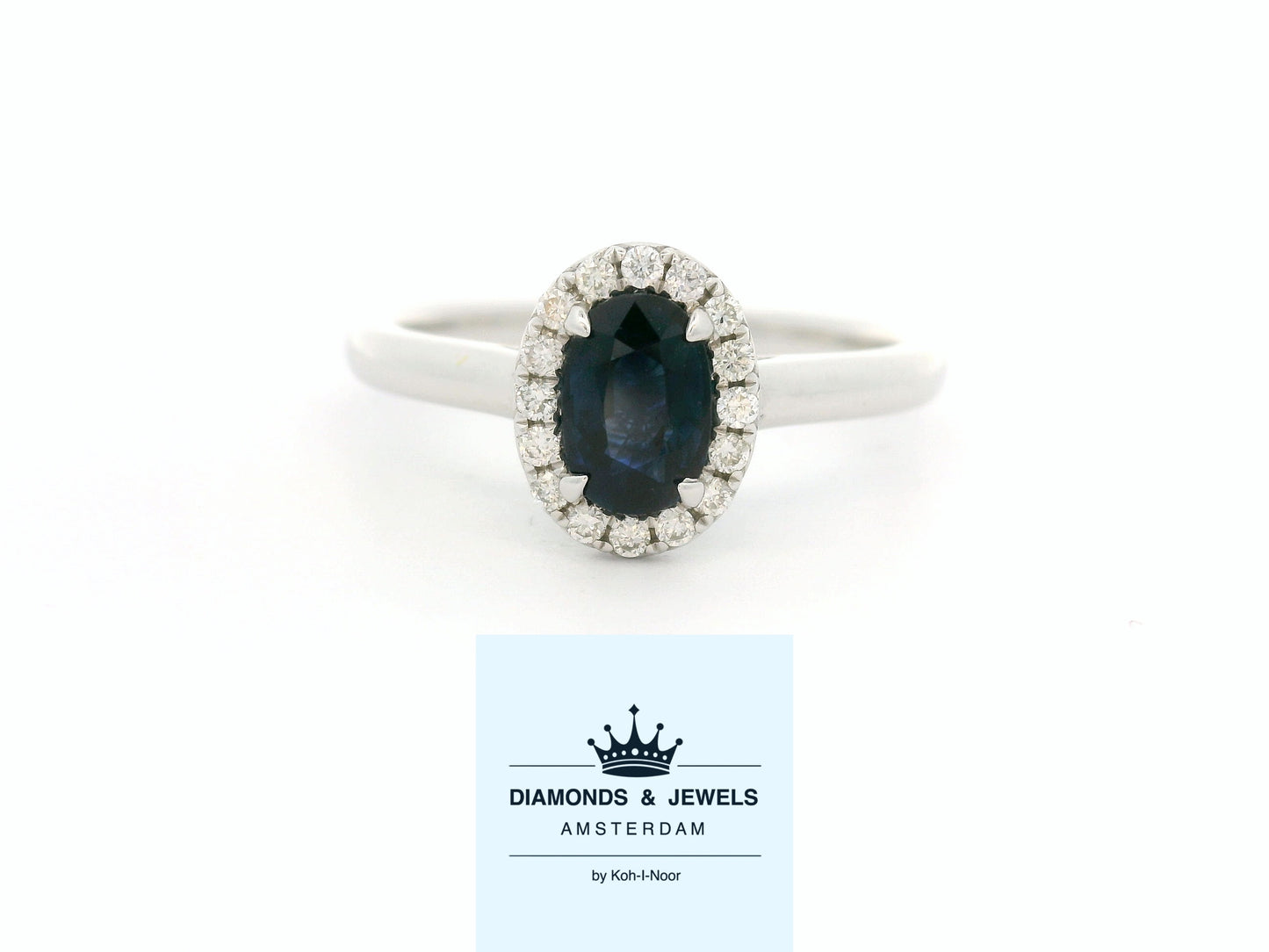 18 karaat witgouden Halo rozet ring van 2.74 gram. Bezet met 1 ovaal geslepen saffier van 0.80 crt en 16 briljant geslepen diamanten met een totaalgewicht van 0.12 crt. Kleur: G Kwaliteit: VS Zetting: 9 x 7 mm Model: R 10448