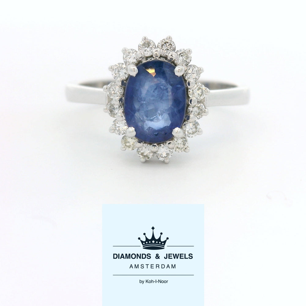 18 karaat witgouden rozetring van 3.3 gram. en 2.5 mm breed. Bezet met 1 ovaal geslepen saffier van 1.10 crt. en 16 briljant geslepen diamanten met een totaalgewicht van 0.16 crt. Kleur:G Kwaliteit: SI2 Zetting:11 x 9 mm Model: R 10543