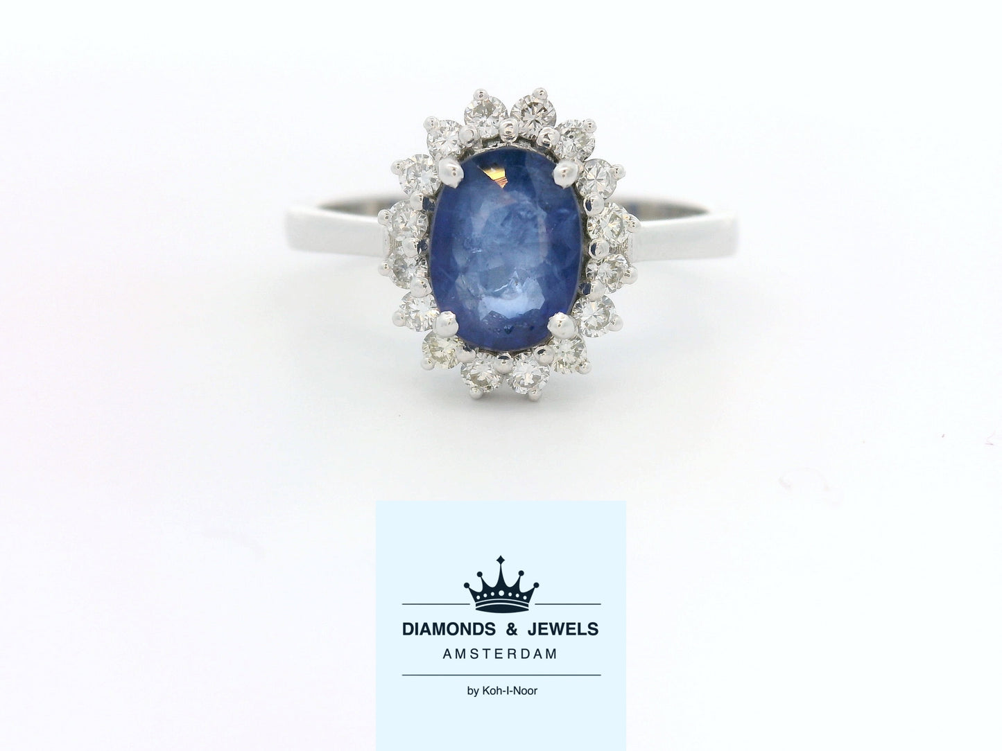 18 karaat witgouden rozetring van 3.3 gram. en 2.5 mm breed. Bezet met 1 ovaal geslepen saffier van 1.10 crt. en 16 briljant geslepen diamanten met een totaalgewicht van 0.16 crt. Kleur:G Kwaliteit: SI2 Zetting:11 x 9 mm Model: R 10543