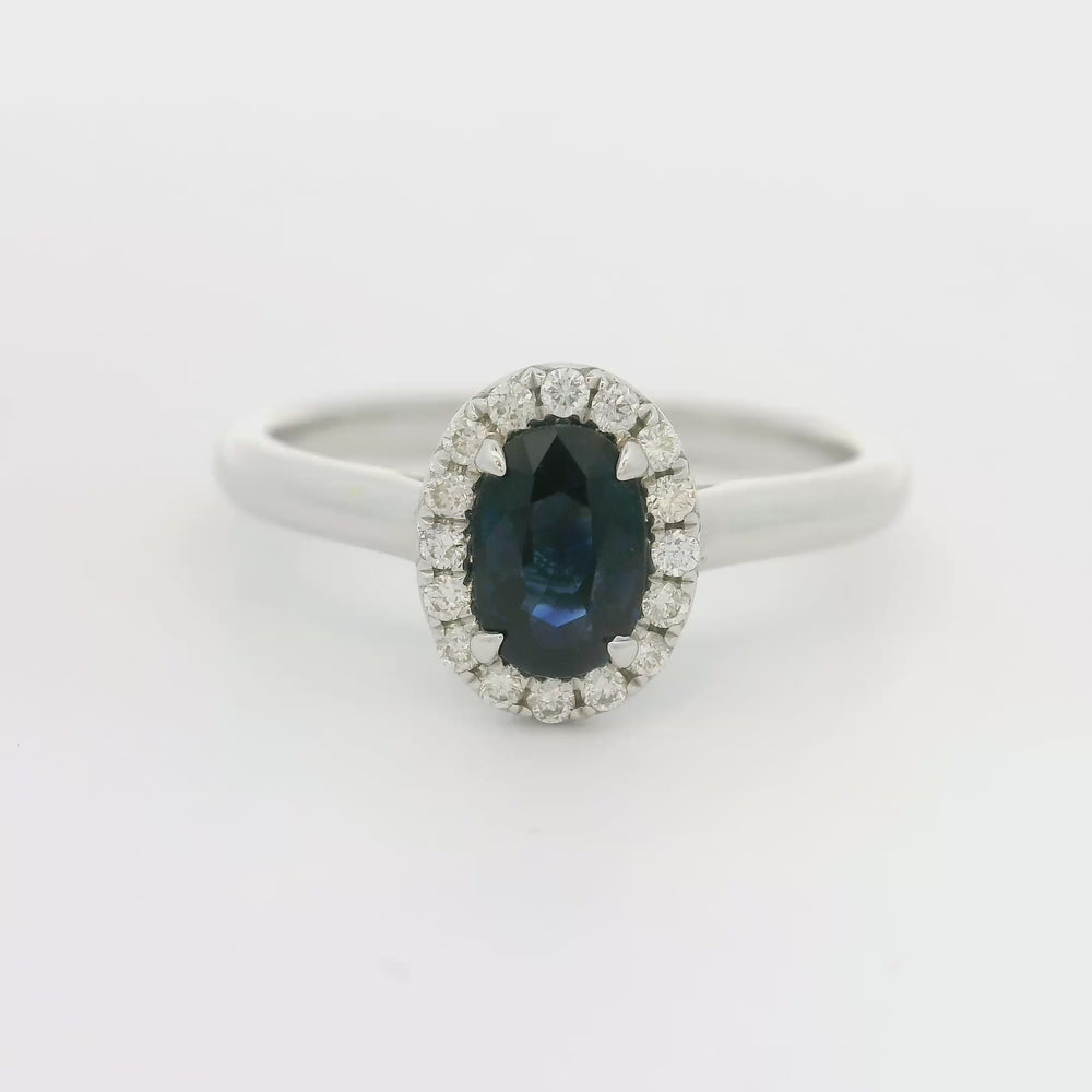 
                      
                        Laad en speel video in Galerijweergave, 18 karaat witgouden Halo rozet ring van 2.74 gram. Bezet met 1 ovaal geslepen saffier van 0.80 crt en 16 briljant geslepen diamanten met een totaalgewicht van 0.12 crt. Kleur: G Kwaliteit: VS Zetting: 9 x 7 mm Model: R 10448
                      
                    