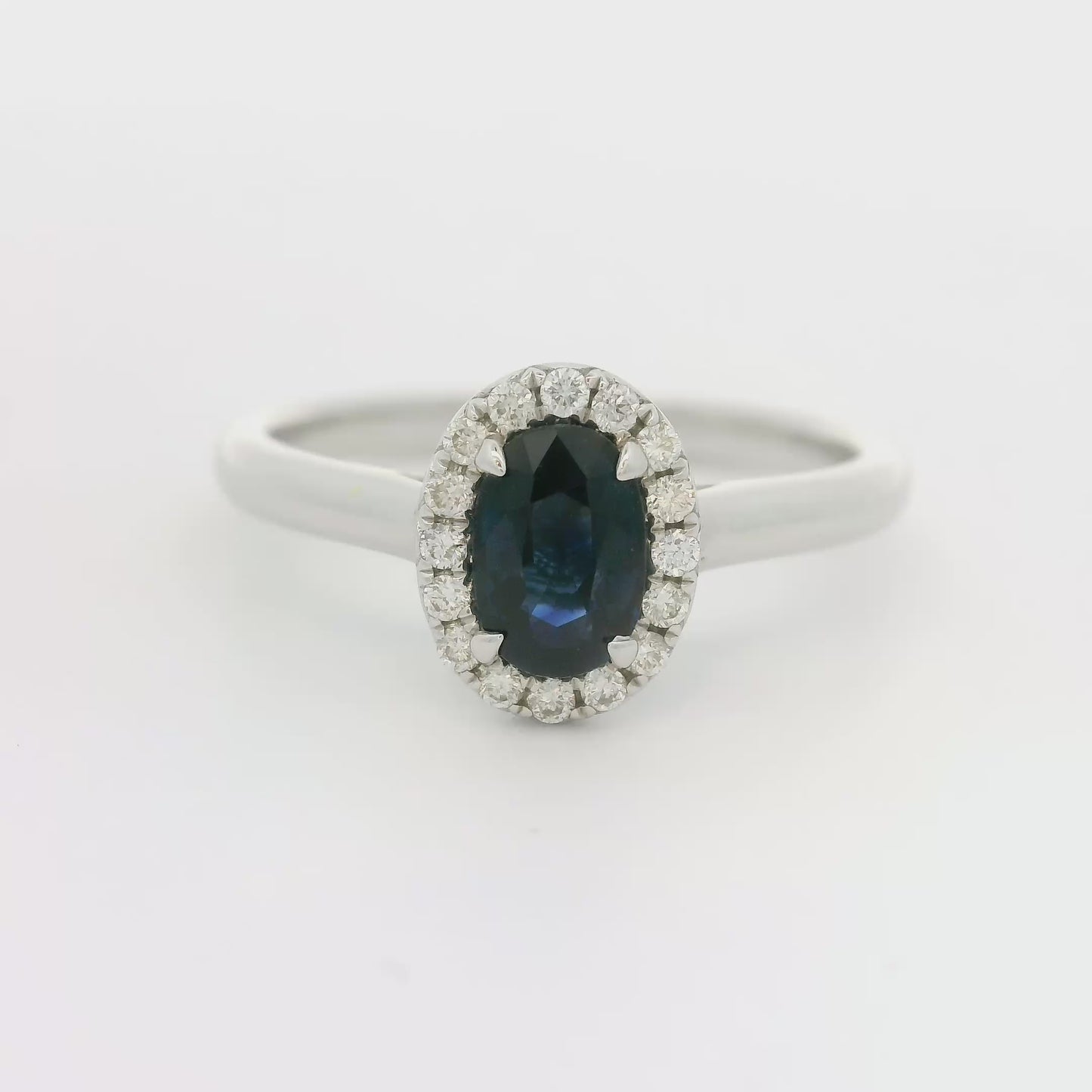 18 karaat witgouden Halo rozet ring van 2.74 gram. Bezet met 1 ovaal geslepen saffier van 0.80 crt en 16 briljant geslepen diamanten met een totaalgewicht van 0.12 crt. Kleur: G Kwaliteit: VS Zetting: 9 x 7 mm Model: R 10448