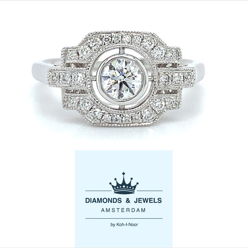 18 karaats witgouden Art Deco ring van 3.7 gram en 2 mm breed. Bezet met 1 briljant geslepen diamant van 0.17 crt en 27 briljant geslepen diamanten met een totaalgewicht van 0.27 crt Kleur: Top Wesselton Kwaliteit: VS Zetting: 10 x 16 mm Model R 9705